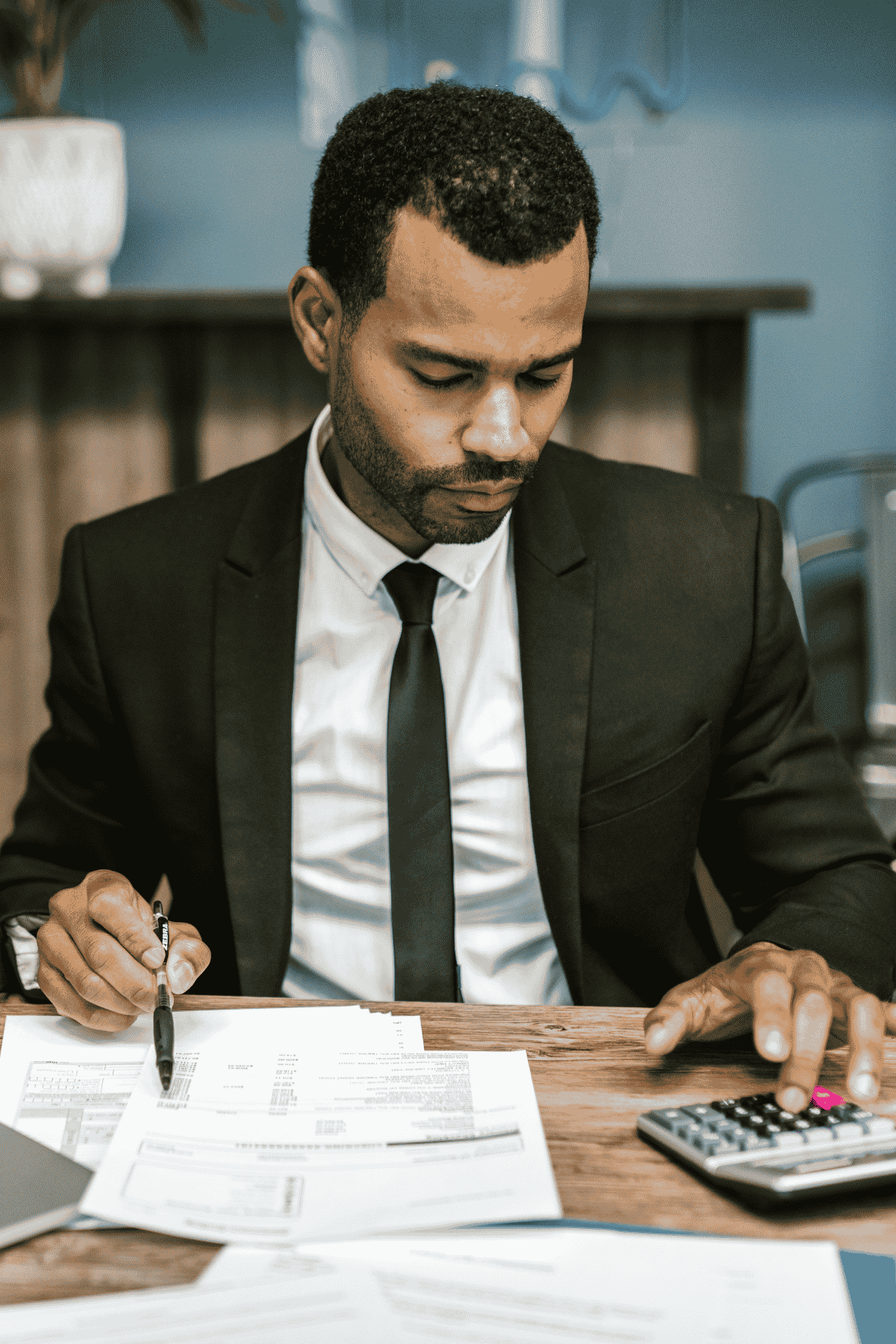 Male accountant writing on paperwork and using calculator at desk
