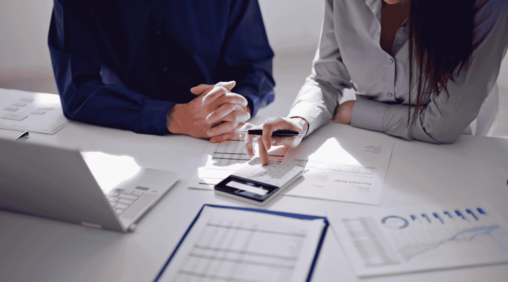 Two professionals using calculator and reviewing financial charts at desk