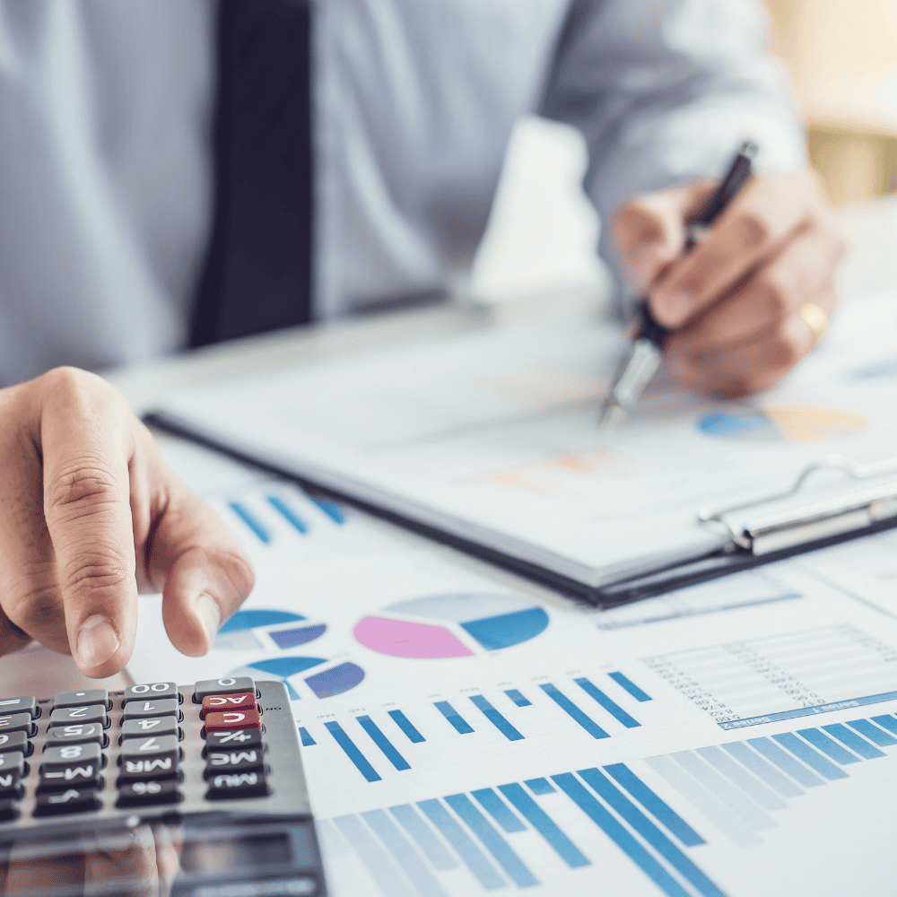 Hands using calculator and pen while reviewing printed financial charts